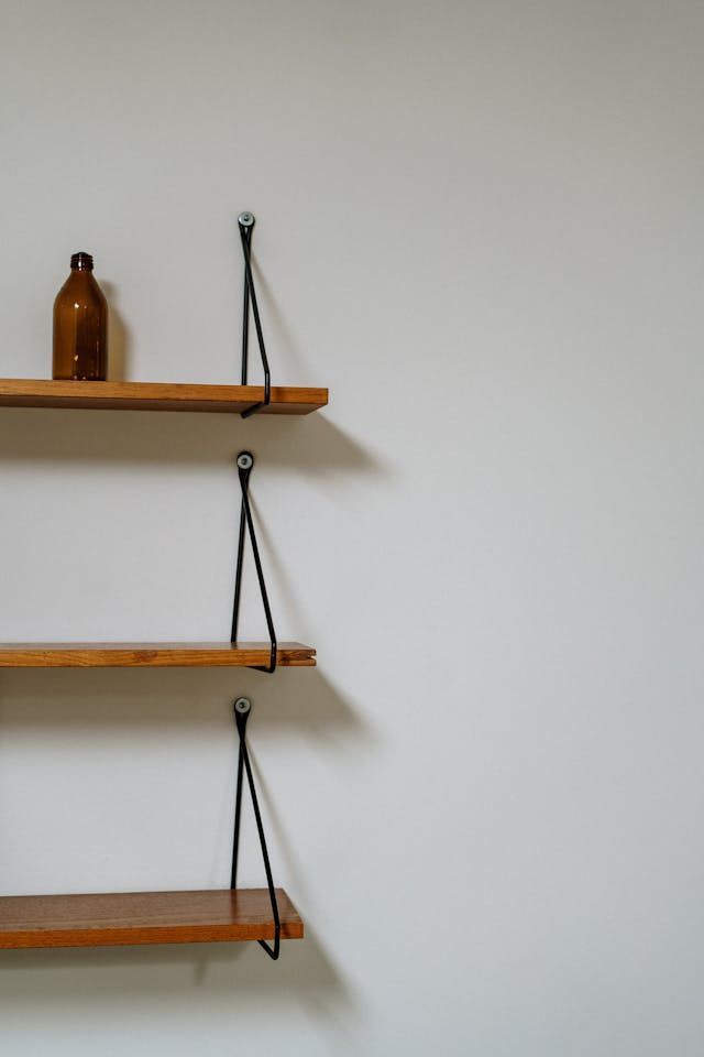 A wooden shelf with a bottle on top of it against a white wall.