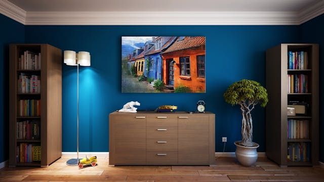 A living room with blue walls , a dresser , a lamp , and a painting on the wall.
