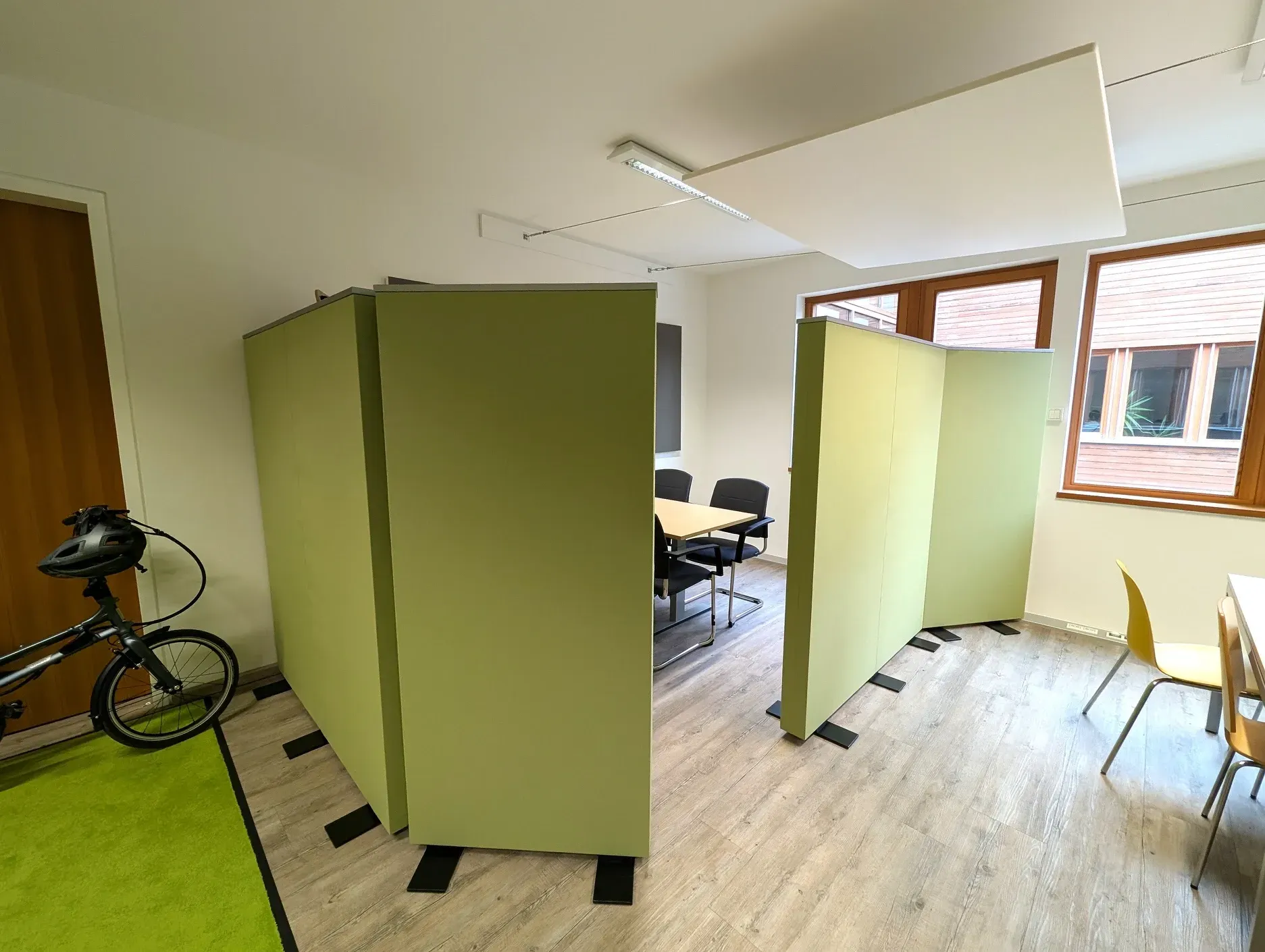 Büroräume mit Trennwänden, Fahrrad, Tischen, Stühlen und Fenstern.