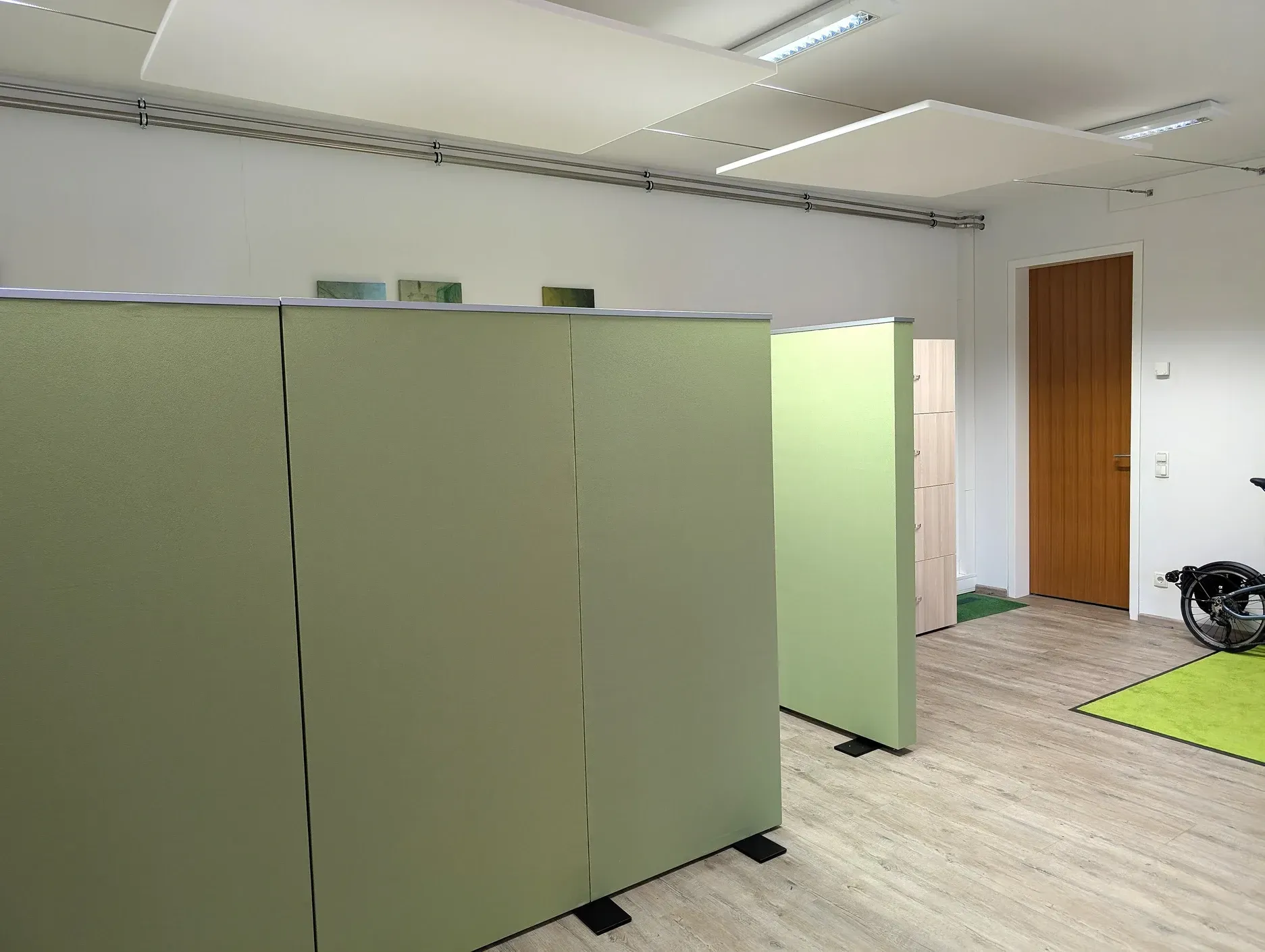 Büroräume mit hellgrünen Trennwänden, einer Holztür und Fliesenboden.