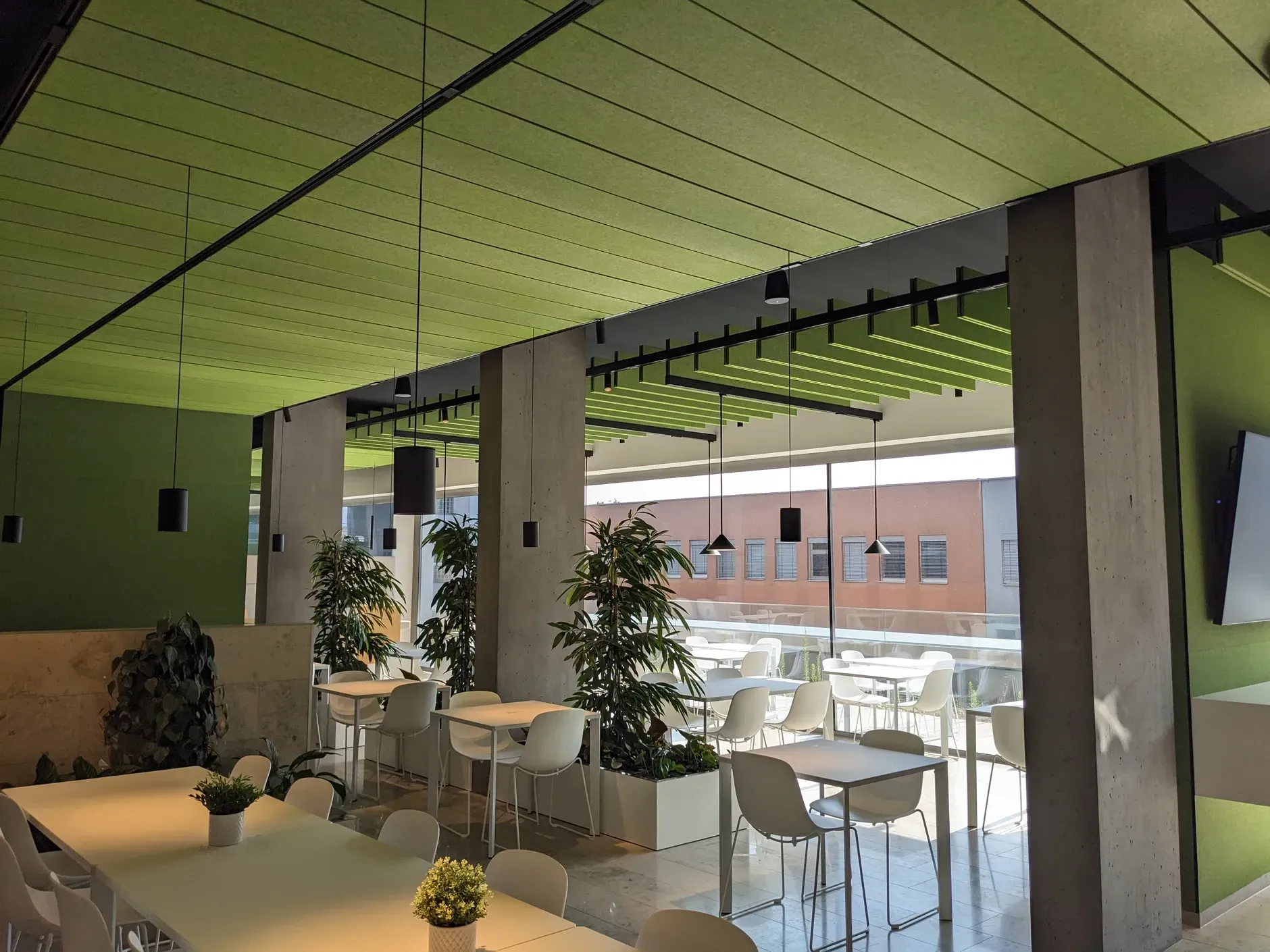 Ein modernes Café mit weißen Tischen und Stühlen, grüner Decke und Blick auf das Stadtbild sowie einer Akustik Wand
