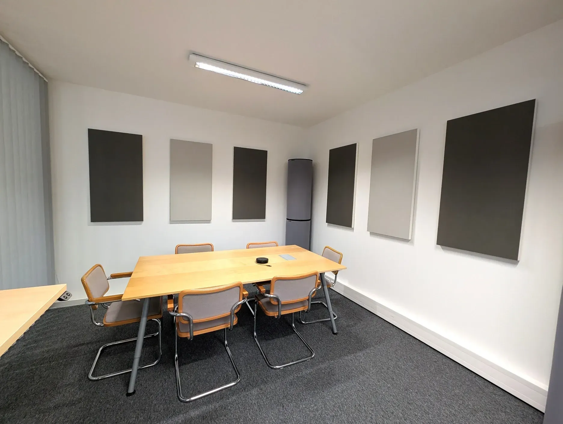 Konferenzraum mit Holztisch, grauen Stühlen, Akustikpaneelen und Teppichboden.