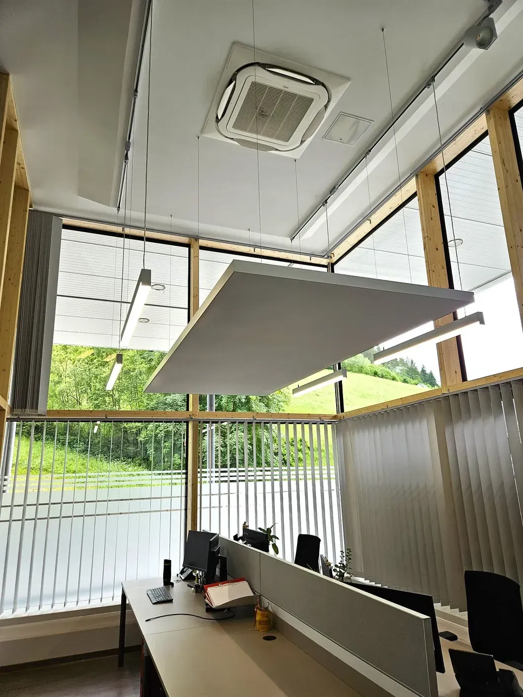 Bürointerieur mit Schreibtischen und großen Fenstern mit Blick ins Grüne; schalldämpfende Paneele hängen von der Decke.