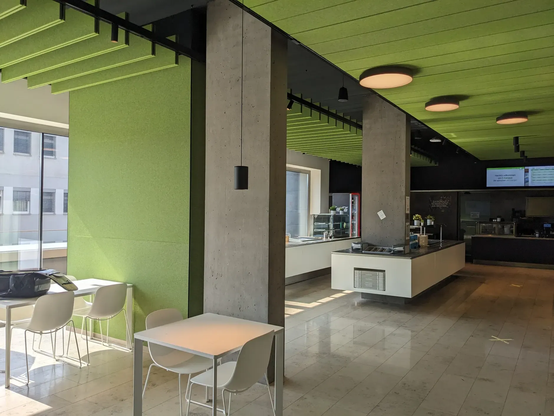 Ein leuchtend grünes Café mit Tischen, Stühlen, Betonsäulen und einer Theke.
