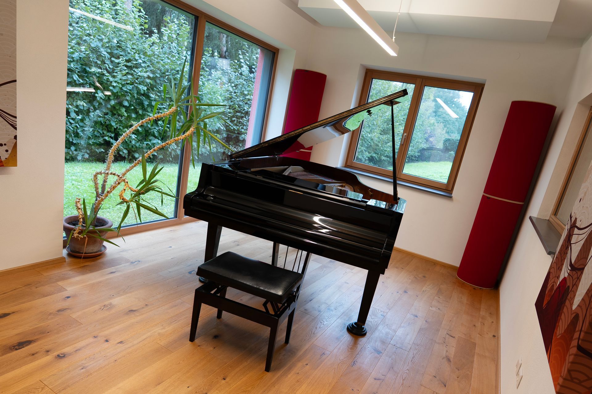 Schwarzer Flügel mit geöffnetem Deckel in einem Raum mit Gartenblick, Holzboden und zwei roten Schallabsorbern.