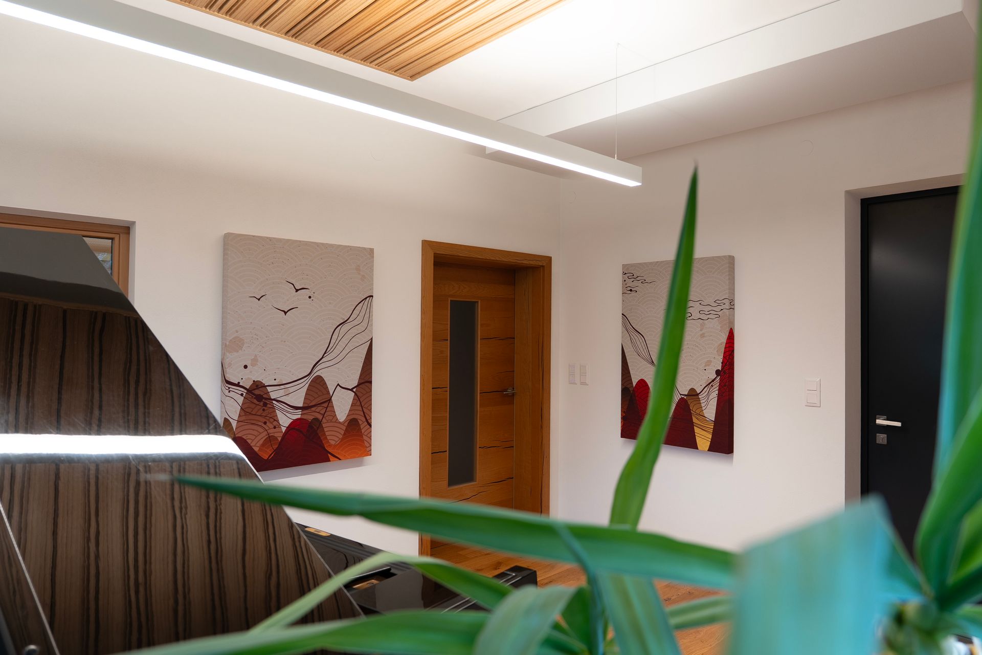 Hell erleuchteter Flur mit Kunstwerken, einer Holztür und einer Pflanze im Vordergrund.