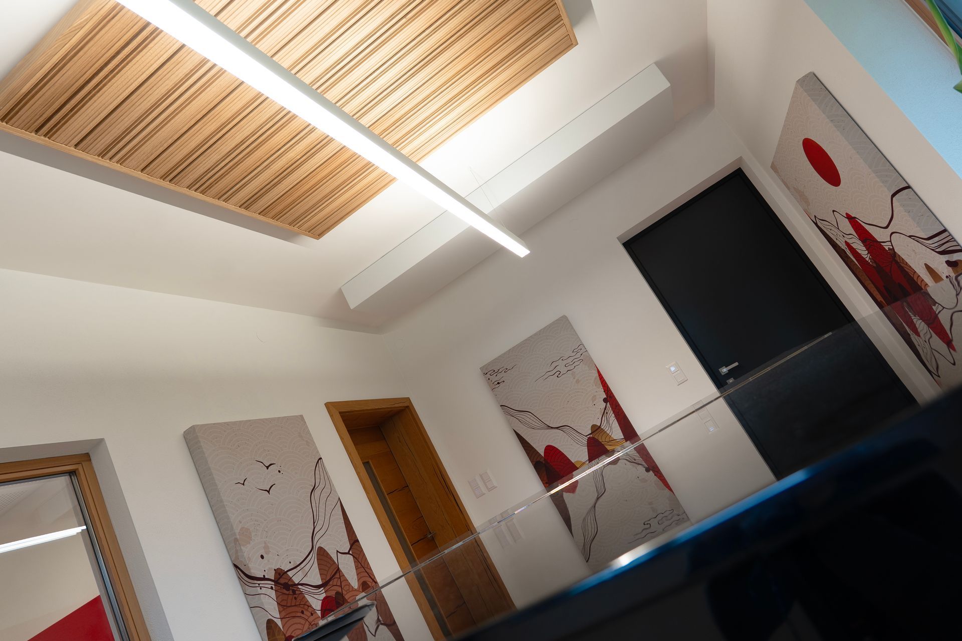 Flur mit moderner Kunst und Holzelementen, beleuchtet von einer langen Deckenleuchte.