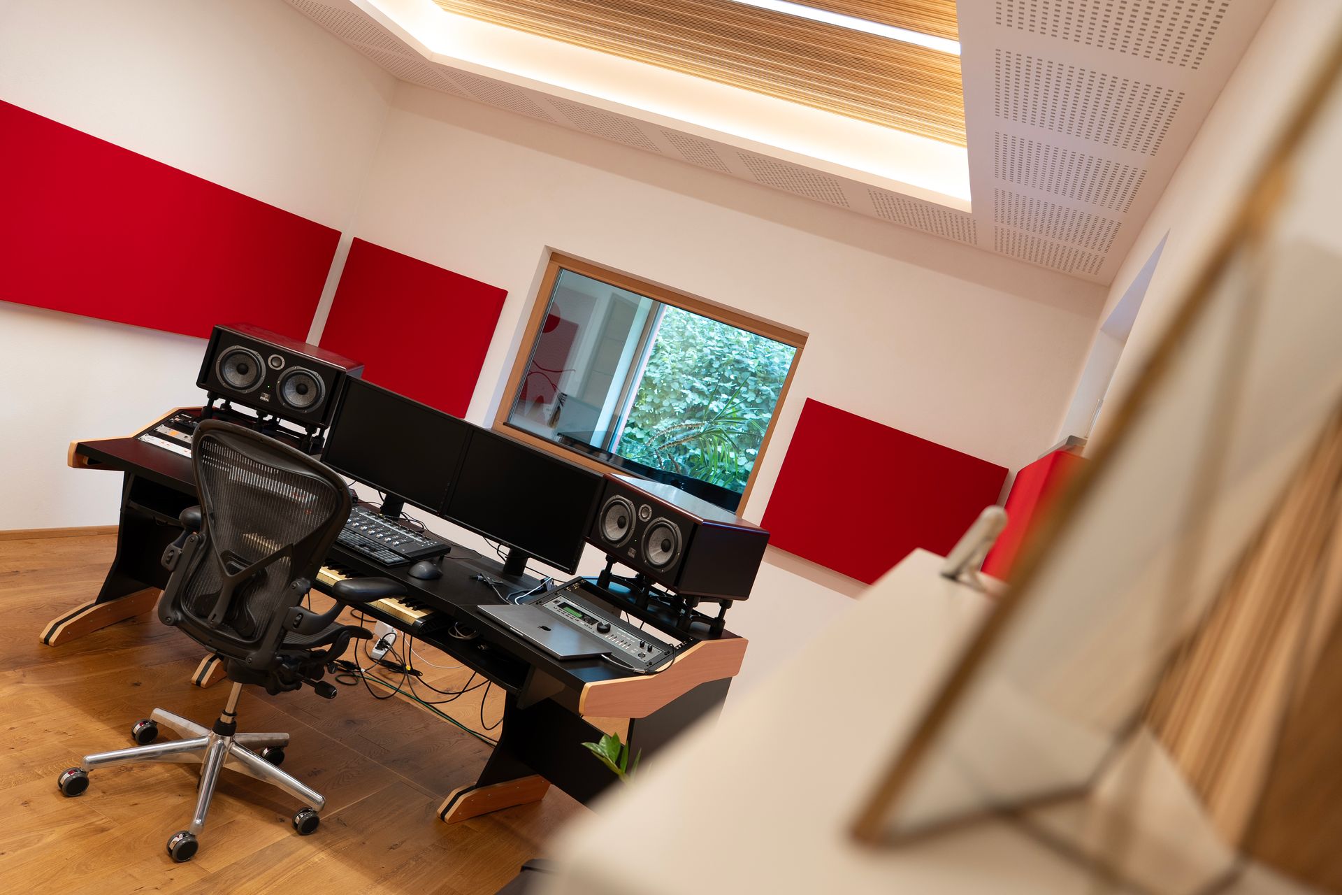 Tonstudio mit Mischpult, Monitoren, Akustikpaneelen, Fenster nach draußen und Bürostuhl.