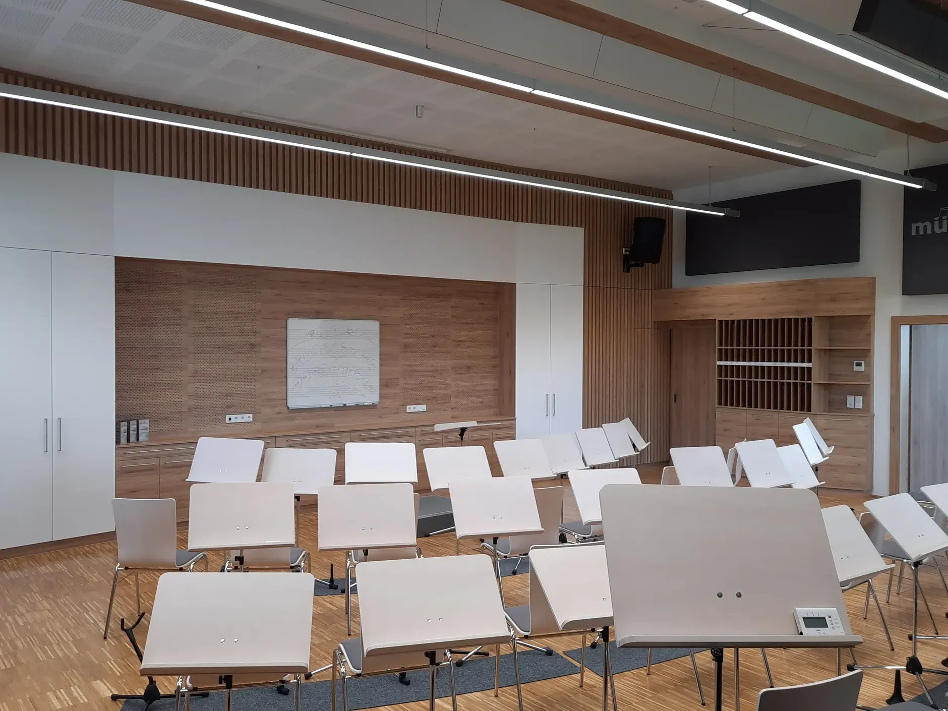 Leerer Probenraum mit Akustikpaneelen Notenständern und Stühlen, die auf eine Bühne mit einer Tafel ausgerichtet sind.