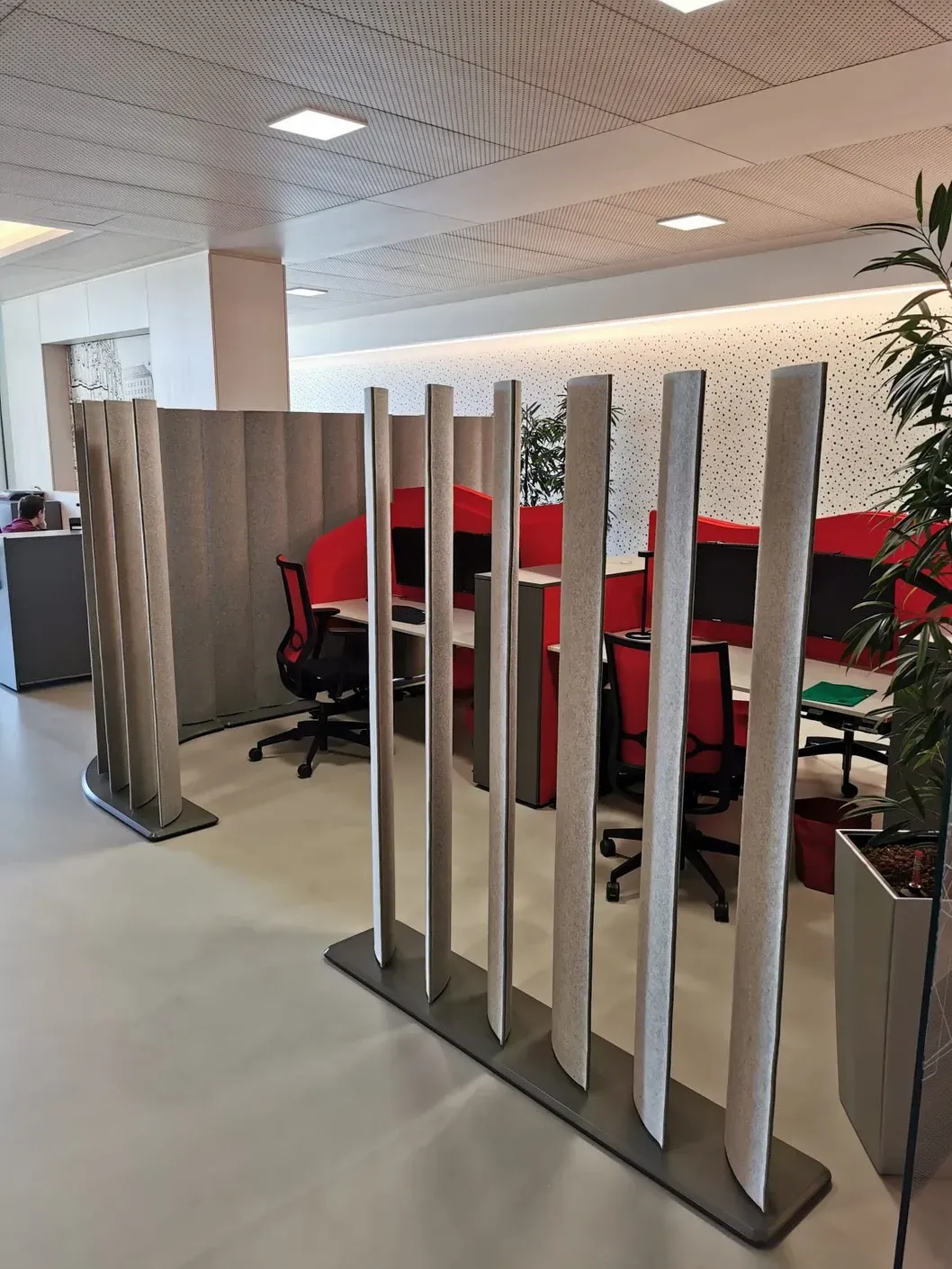 Modernes Büro mit grauen Akustik Trennwänden, roten Stühlen und weißer Decke mit dekorativen Mustern.