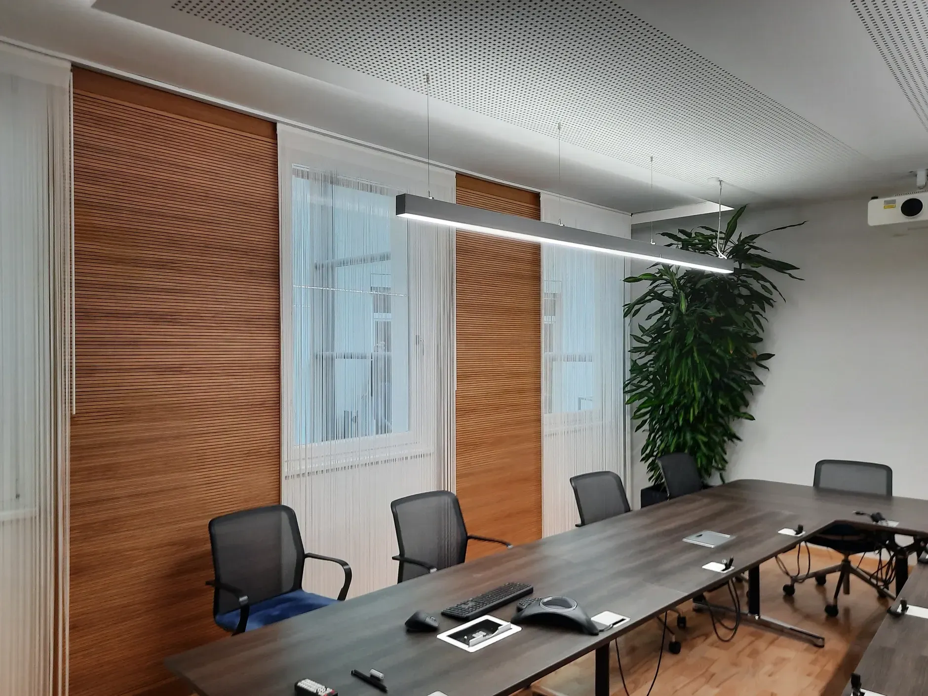 Konferenzraum mit Akustik Wand Holzvertäfelung, langem Tisch, Stühlen, Fenstern und dekorativer Decke.