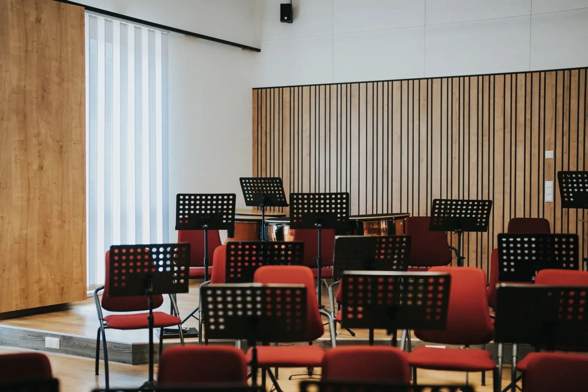 Leerer Musikprobenraum mit Akustikpaneelen mit roten Stühlen, Notenständern und Holzvertäfelung.