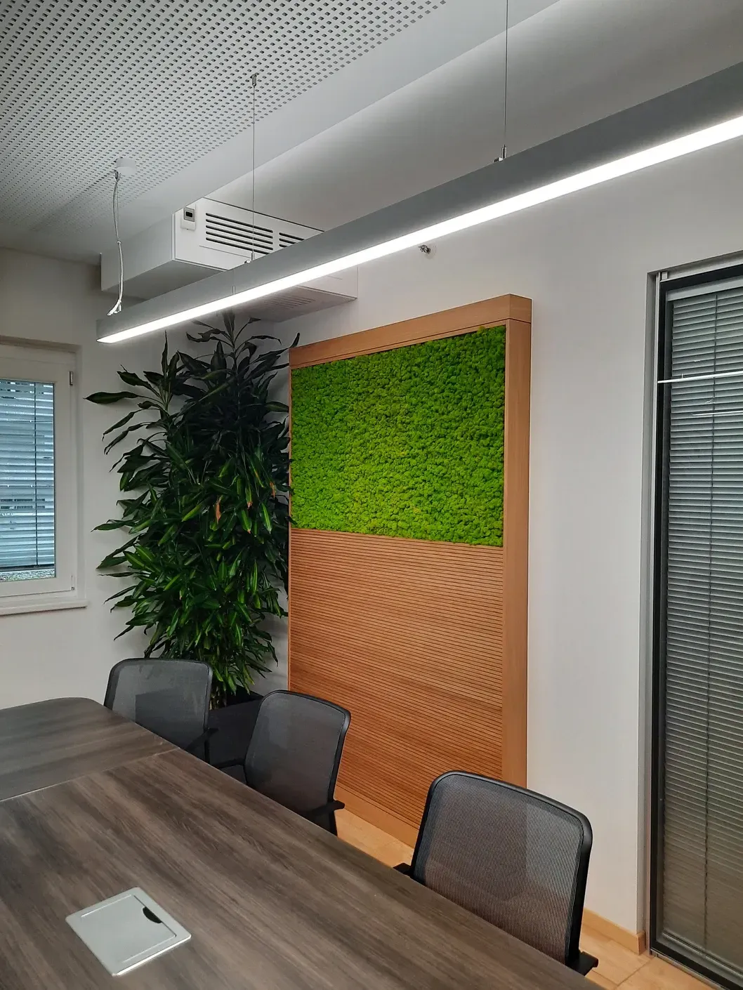 Konferenzraum mit Akustikwand aus Holz und Grün, langem Tisch, Stühlen und natürlichem Licht.