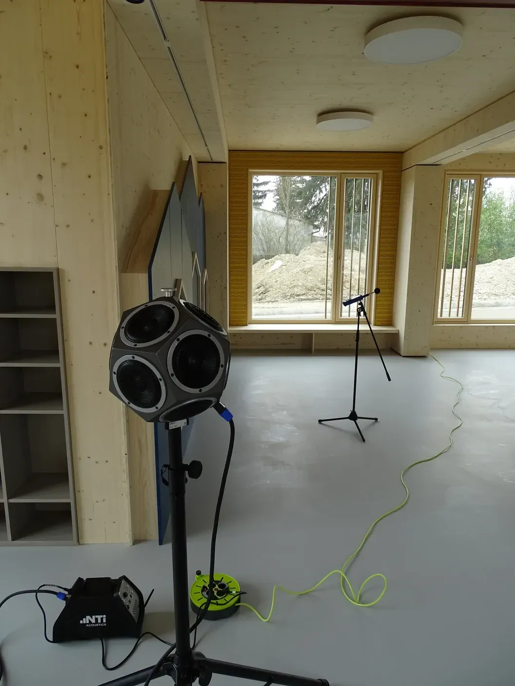 Akustischer Messaufbau in einem Raum: ein kugelförmiges Mikrofon, Stativ, Kabel und Fenster.