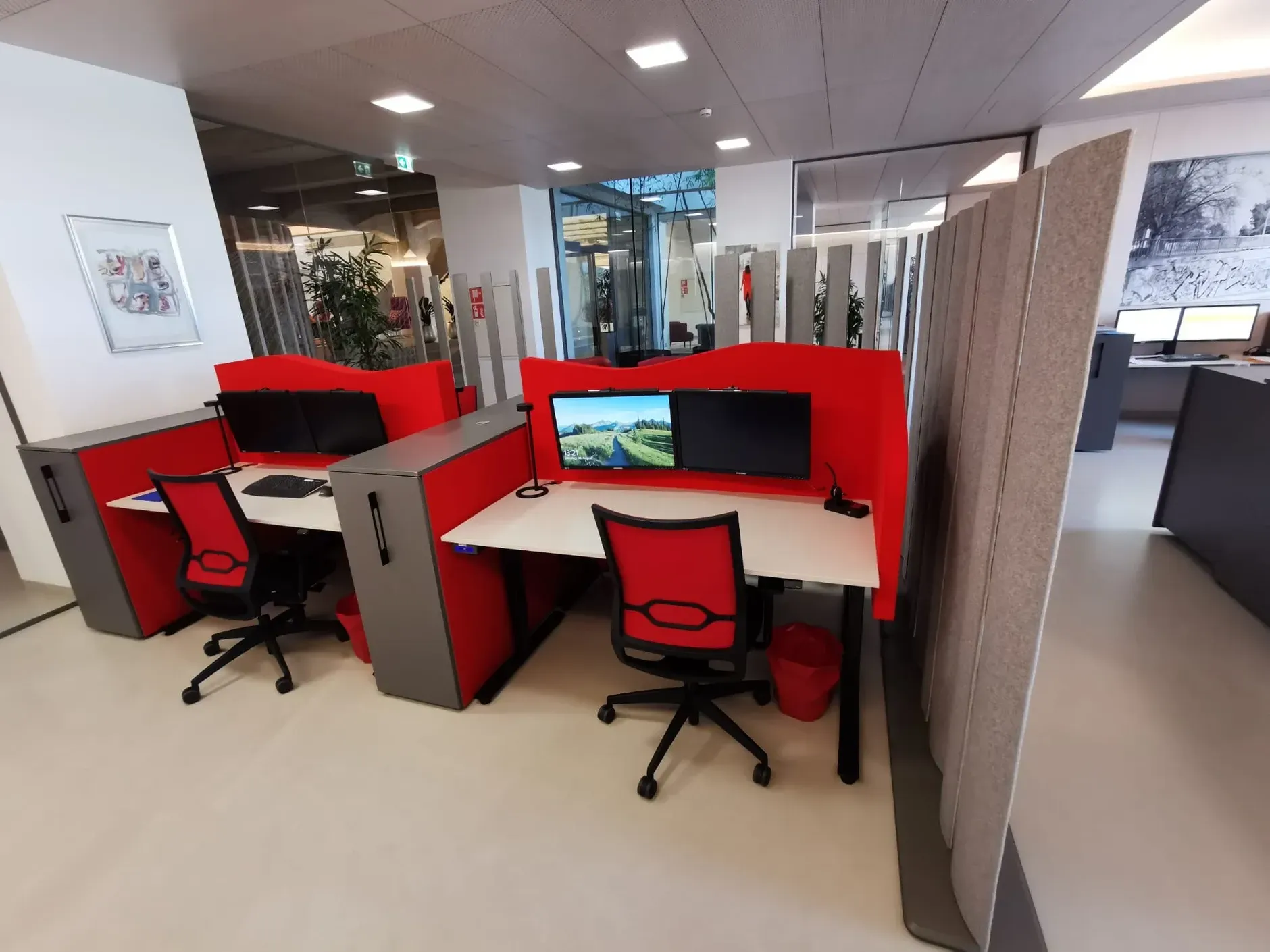 Bürokabinen mit roten und grauen Akustik Wänden, Schreibtischen und Stühlen. Die Schreibtische sind mit Monitoren ausgestattet.