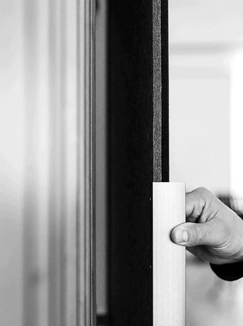 Eine Hand hält einen hellen, rechteckigen Block neben einer dunklen, vertikalen Fläche mit strukturierter Kante.