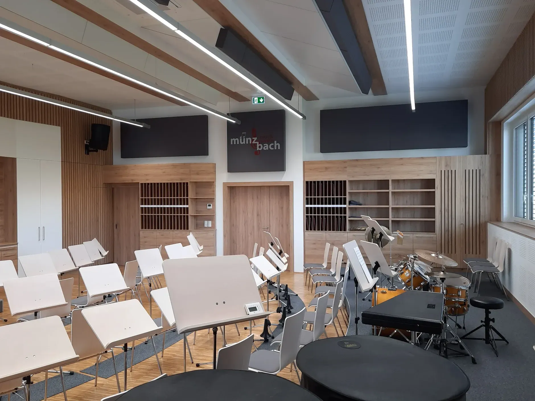 Musikproberaum mit Instrumenten, Stühlen und Notenständern; Wände und Decke aus Holz mit Akustikpaneelen