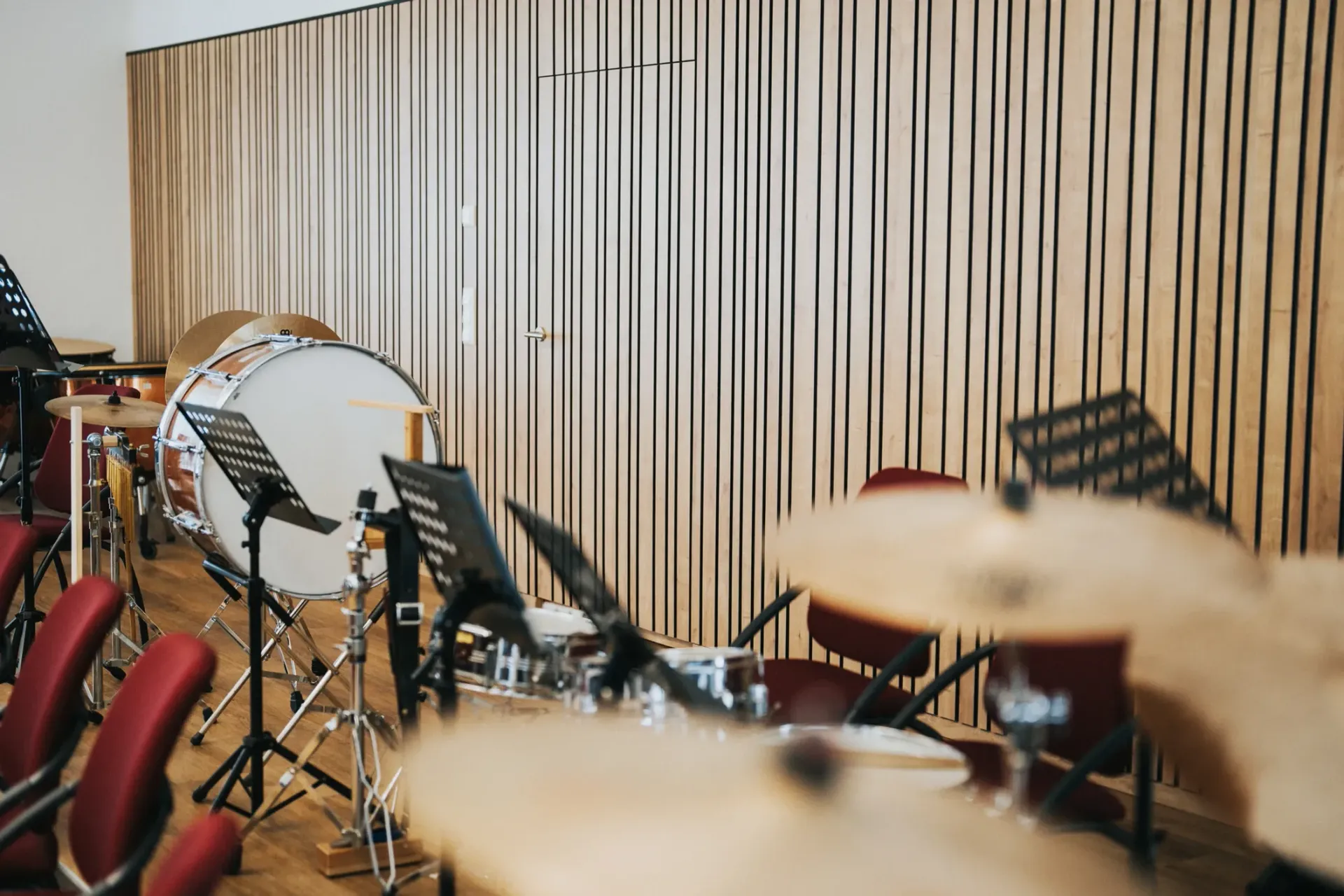 Schlagzeug und Notenständer in einem holzgetäfelten Studio, links sind rote Stühle zu sehen.