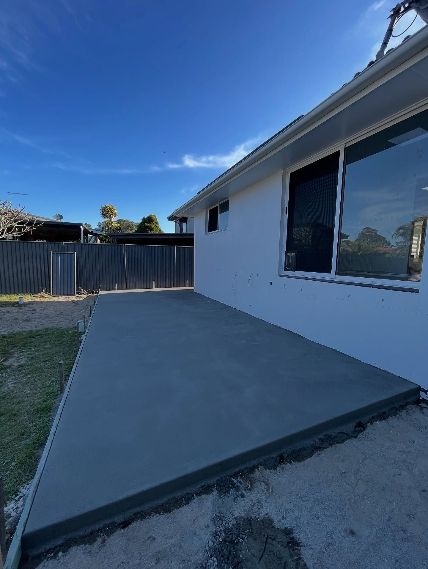 Newly Poured Concrete Patio Next to a White House With a Sliding Glass Door — All Concrete Creations in Robina, QLD