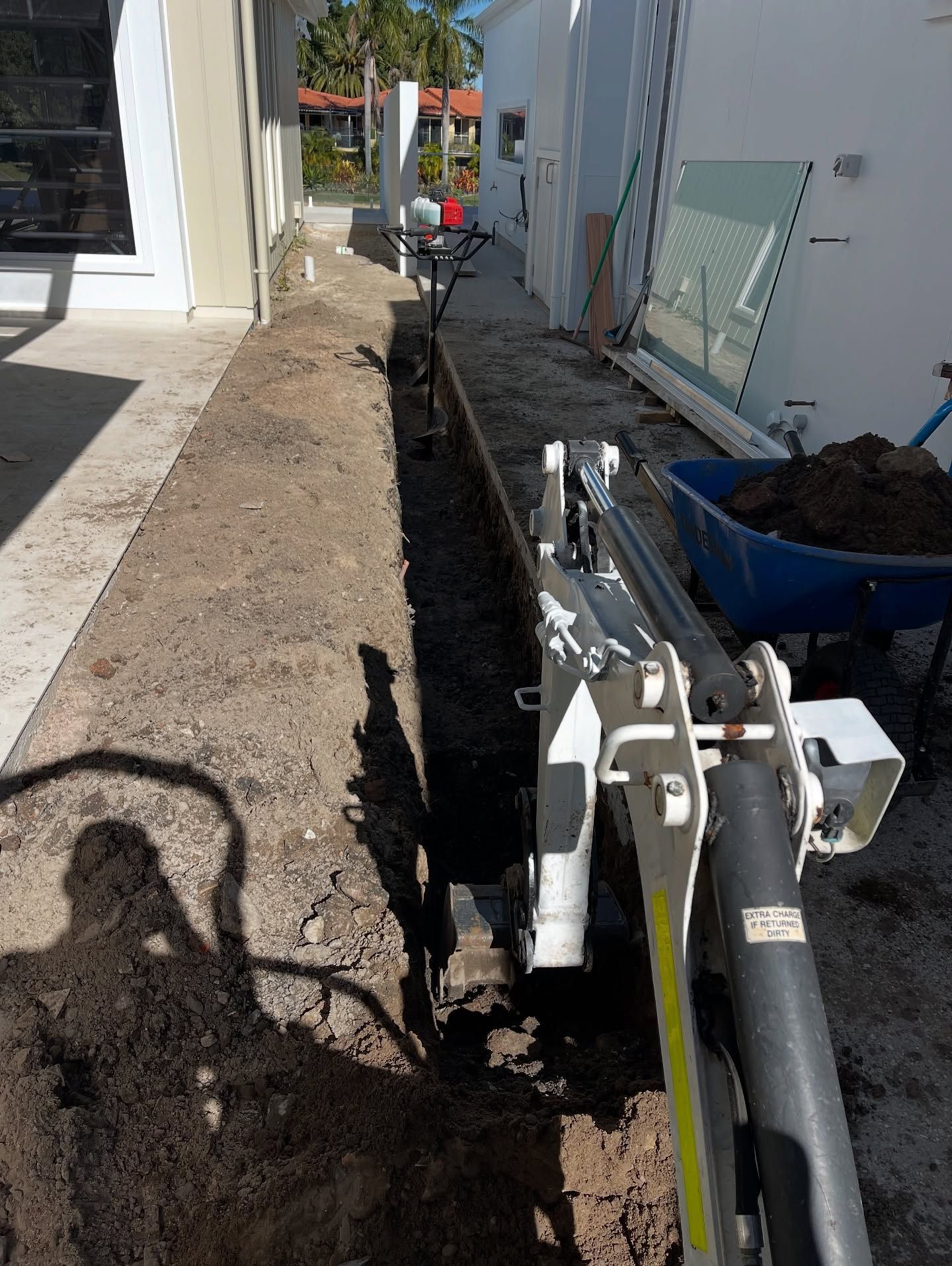 A Small Excavator Digging a Trench Along the Side of a Building — All Concrete Creations in Kingscliff, NSW