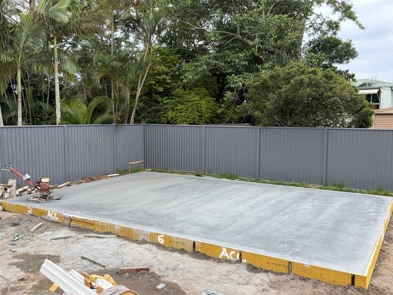 Concrete slab for construction with gray corrugated fence and trees in the background.