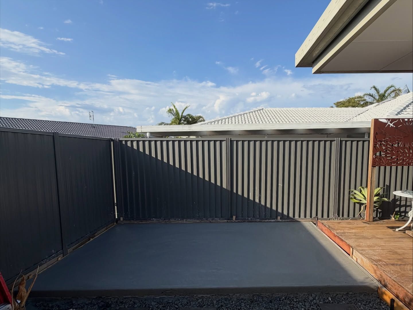 Newly poured concrete slab in backyard, dark gray fence, blue sky — All Concrete Creations in Robina, QLD