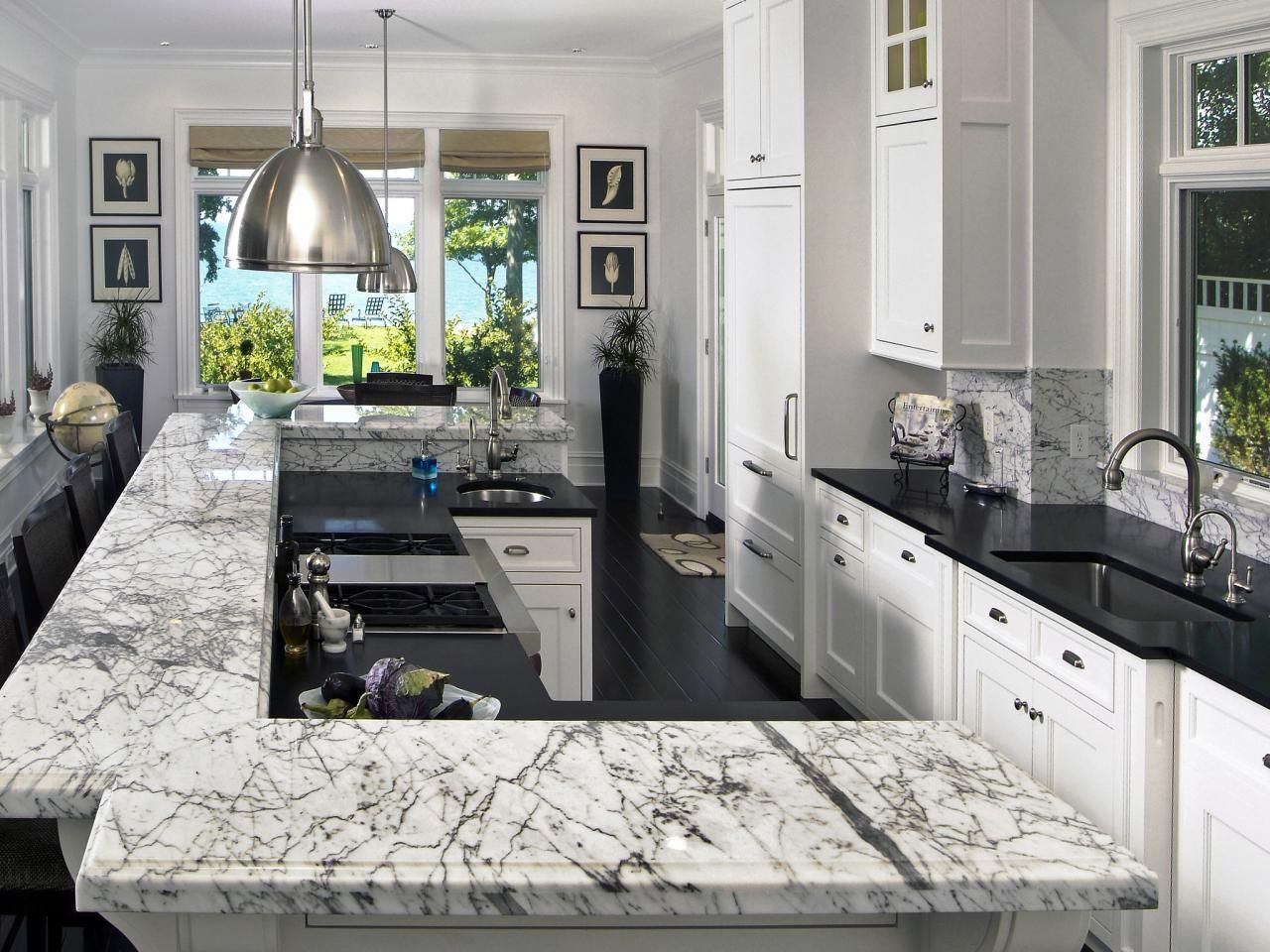 Spacious white kitchen with marble countertops, dark floors, and large windows overlooking water.