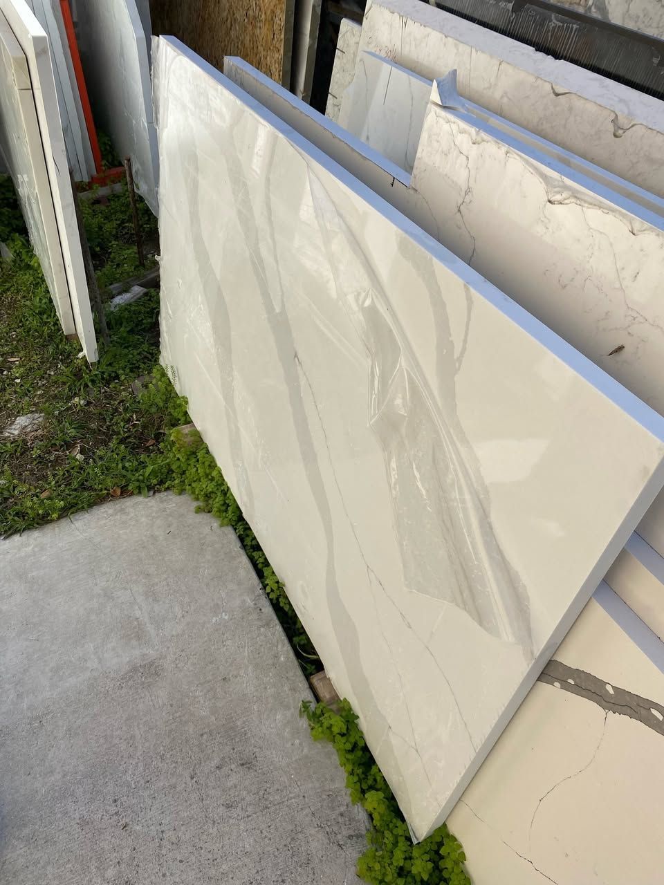 White countertop slabs stacked outside on grass and concrete.