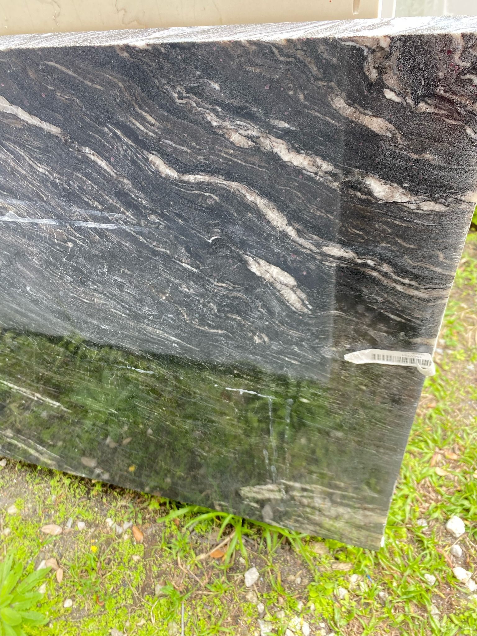 Black granite slab with swirling white and gray patterns, reflecting a green lawn.