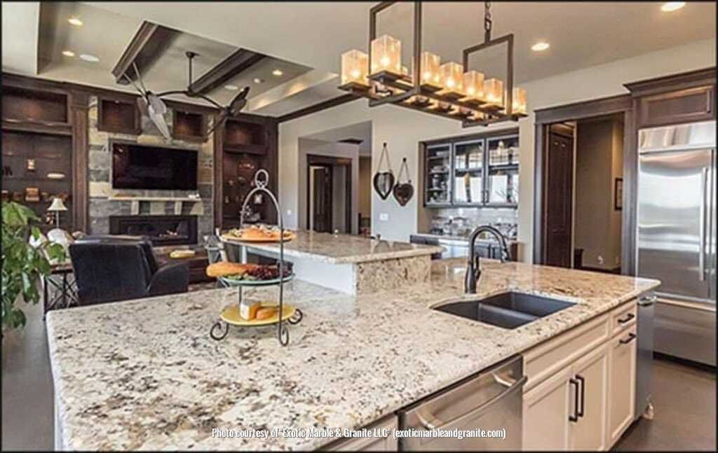 Luxurious kitchen with granite countertops, island, and overhead lighting. Living area visible in background.