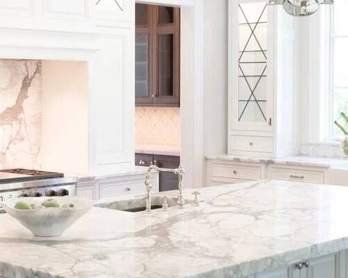 Elegant white kitchen with marble countertops and dark wood cabinetry visible in the background.
