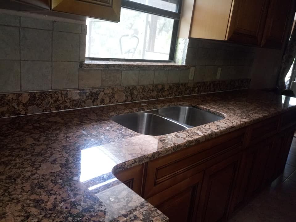 Granite kitchen countertop with a double sink, dark cabinets, and a window.