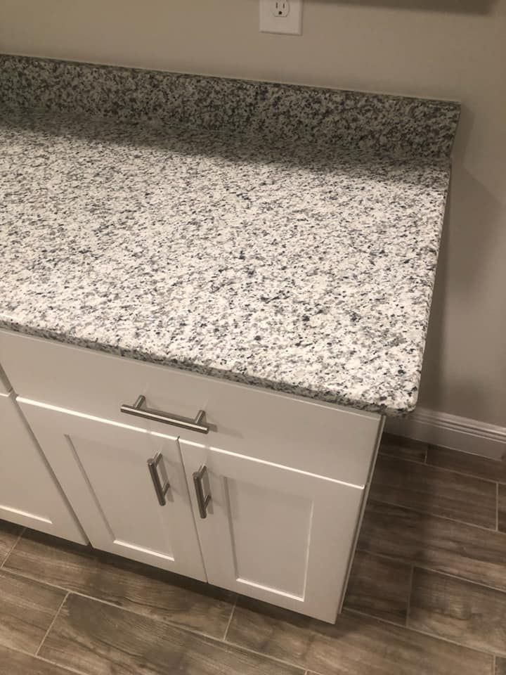 White cabinets with silver handles beneath a gray speckled countertop and wall.