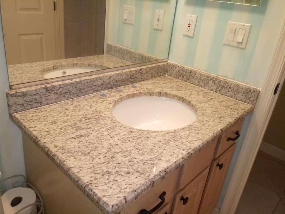 Bathroom vanity with a granite countertop and a round sink, light wood cabinets, and a mirror.