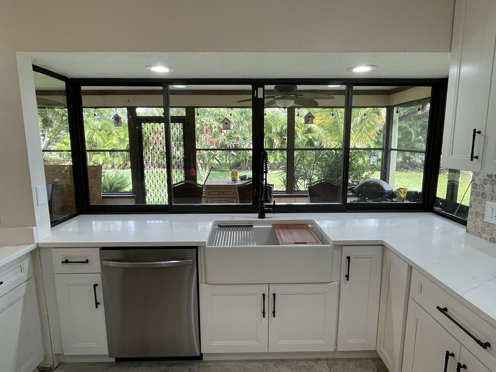 Modern kitchen with white cabinets, stainless steel appliances, and a black-framed window overlooking a backyard.