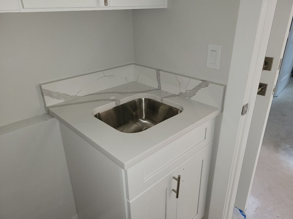 White cabinet with stainless steel sink, gray countertop with a corner backsplash in a neutral-colored room.