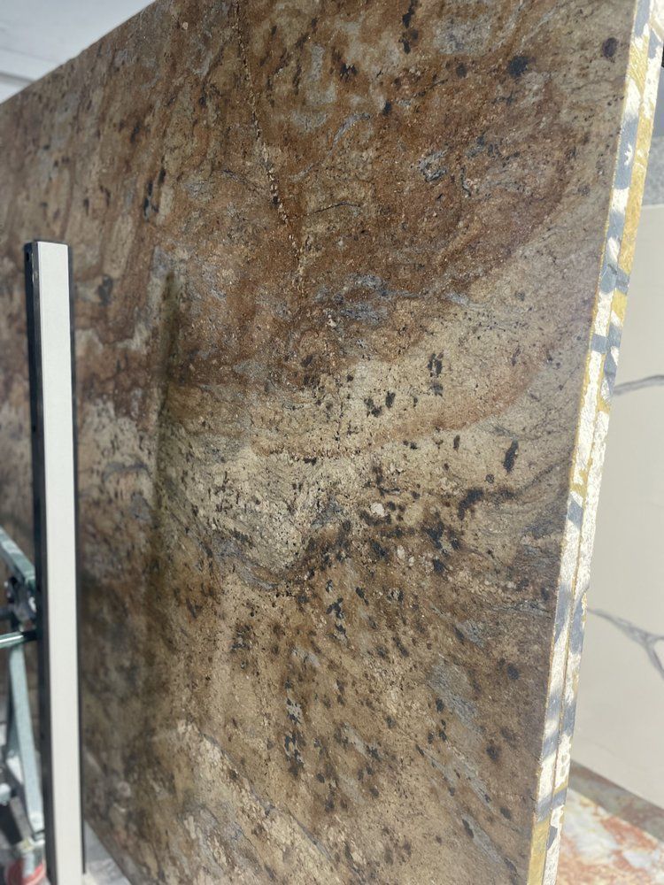 Large granite slab with brown, gold, and black swirling patterns; resting against a wall.