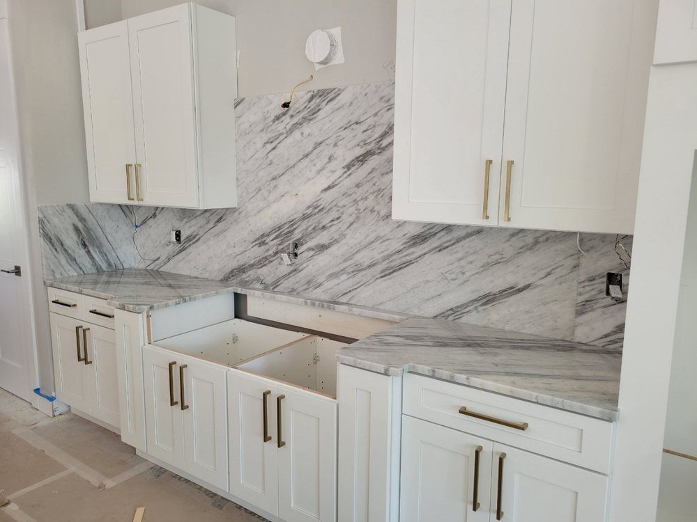 White kitchen cabinets with marble countertops and backsplash, under construction.