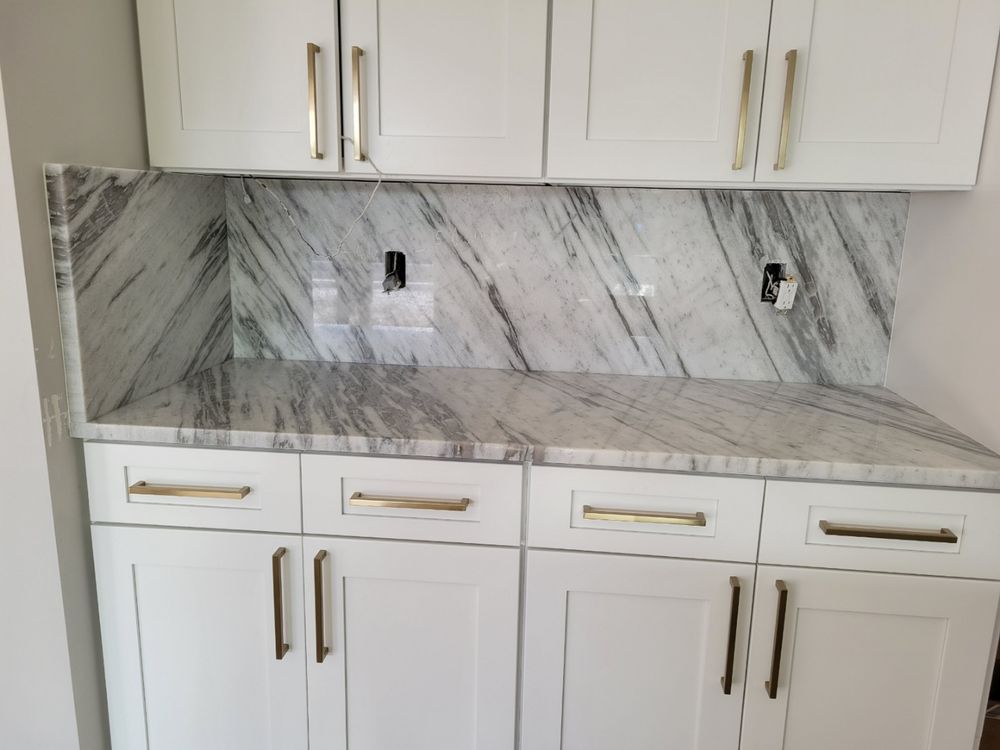 White kitchen cabinets with marble countertop and backsplash, gold hardware.