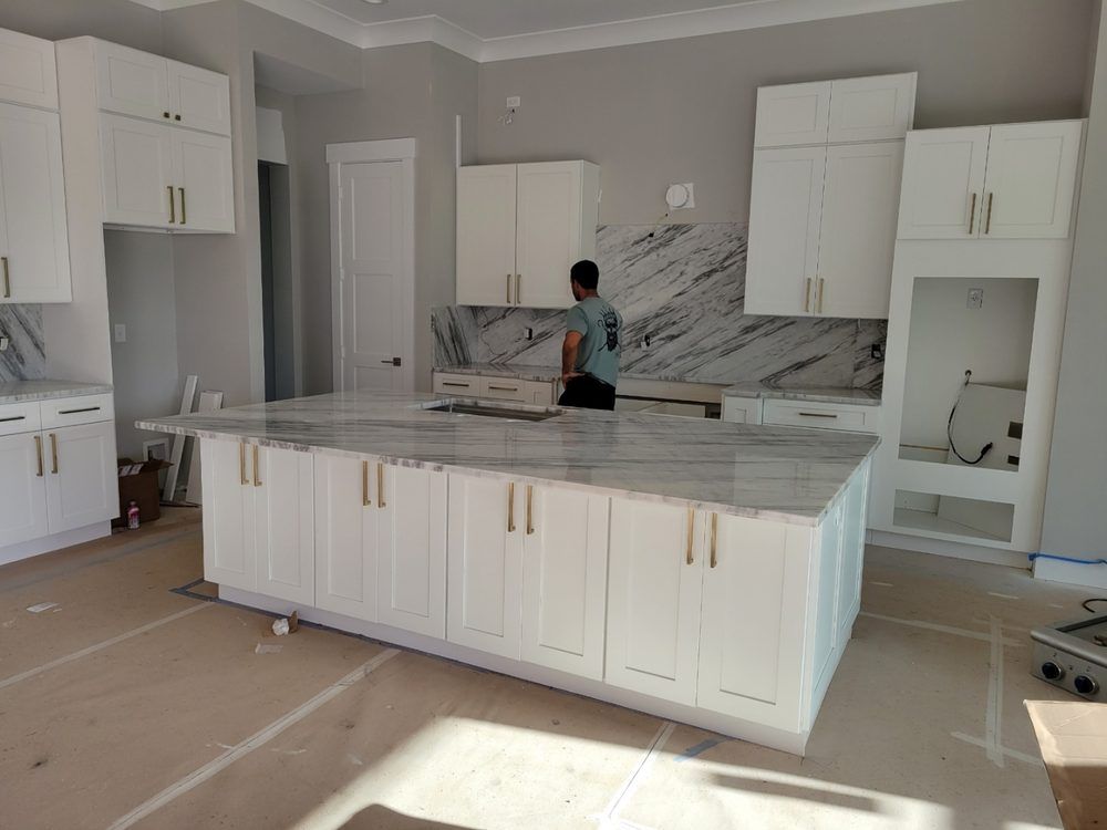 White kitchen with island, marble countertops, cabinets, and a person working.