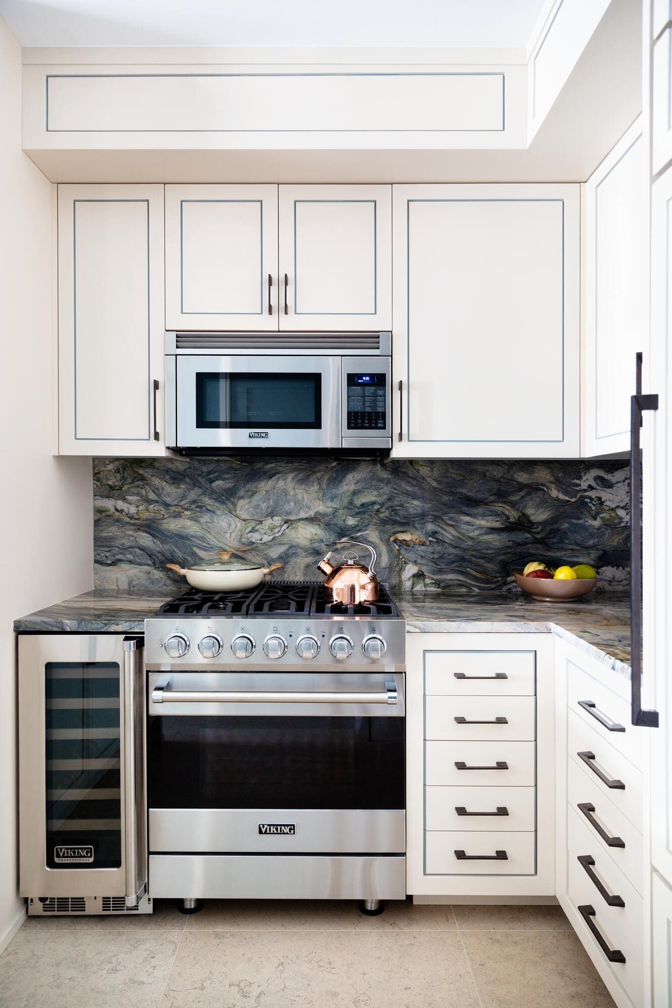 Small, modern kitchen with white cabinets, stainless steel appliances, and a marble backsplash.