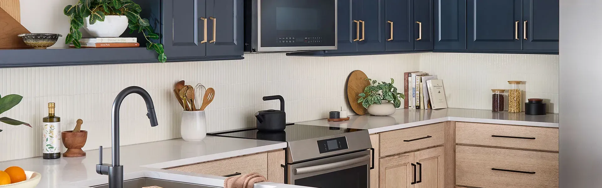 A modern kitchen with blue upper cabinets and wood-toned lower cabinets. Stainless steel appliances and a black faucet.