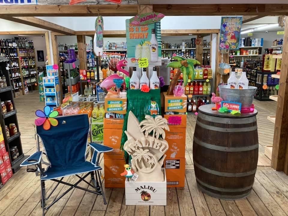 A store display with Malibu rum, tropical decor, a chair, and a barrel, promoting summer drinks.