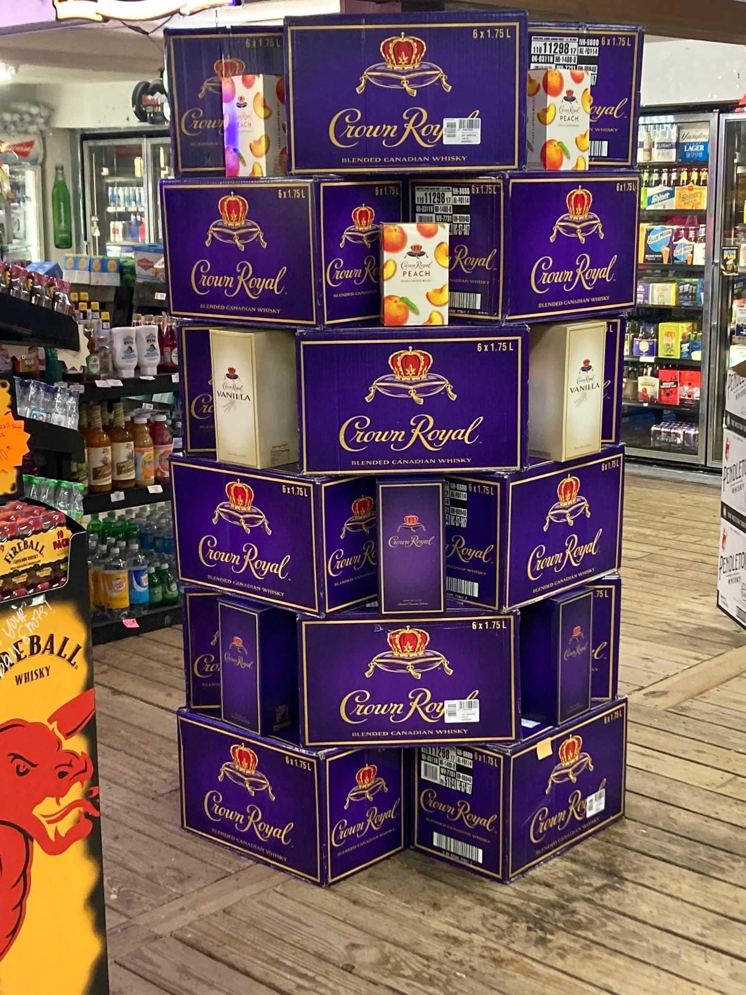 Display of Crown Royal liquor boxes and bottles in a store. Purple boxes with gold lettering are stacked.