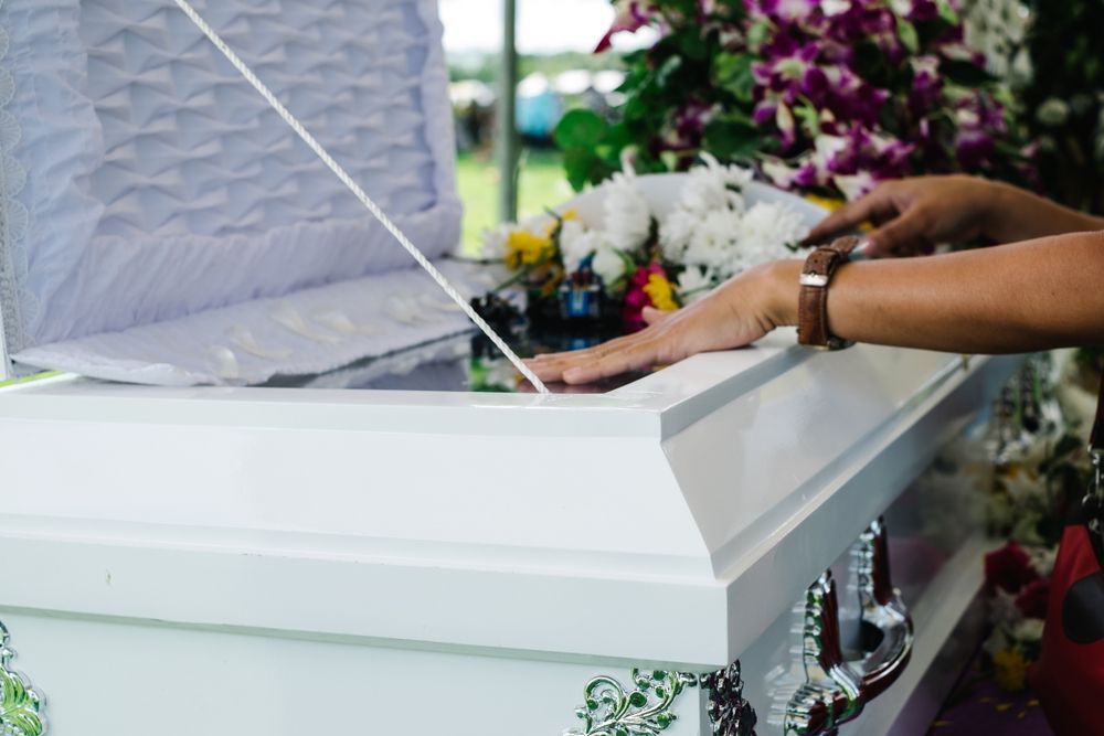 Hands Resting on the Open Lid of a White Casket — Finlayson & McKenzie Funeral Directors in Rockhampton City, QLD