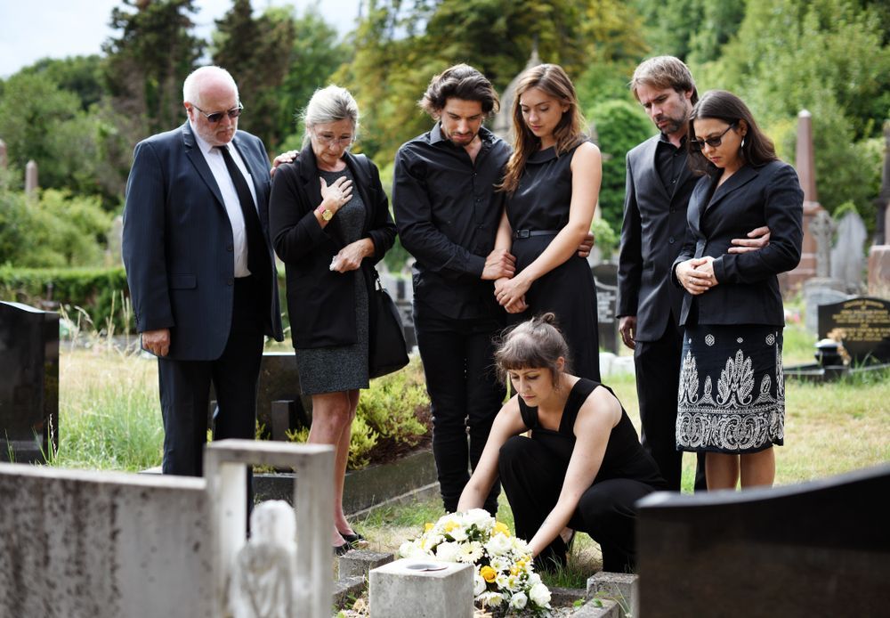 People in Black Clothing at a Graveside, One Placing Flowers — Finlayson & McKenzie Funeral Directors in Yeppoon, QLD