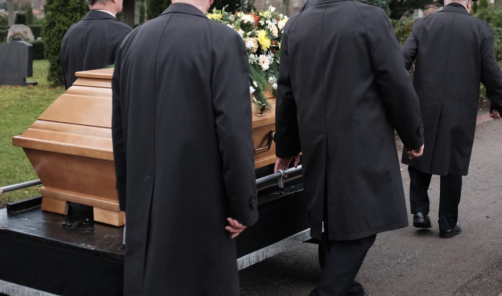 Men in Black Coats Carrying a Wooden Casket at a Cemetery — Finlayson & McKenzie Funeral Directors in Rockhampton City, QLD