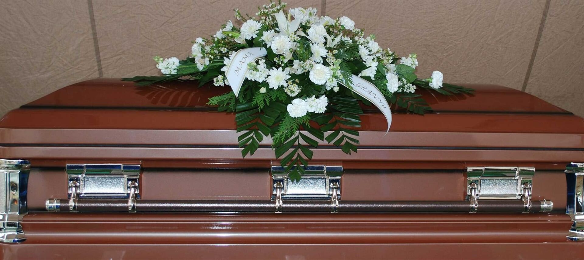 Brown Casket With White Floral Arrangement — Finlayson & McKenzie Funeral Directors in Rockhampton City, QLD