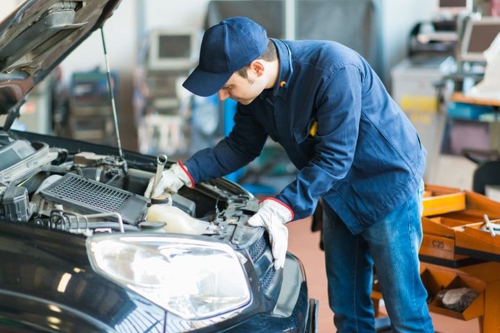 Mechanic in blue uniform inspecting the front of a black car in a garage
