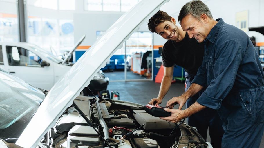 Two mechanics inspecting an open car engine in a bright auto repair shop
